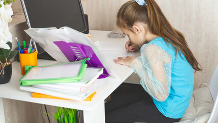 Little school girl sit at table at home write in exercise book prepare homework alone.
