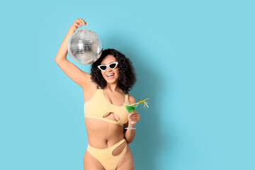 Beautiful woman in swimsuit, with cocktail and with disco ball on blue background