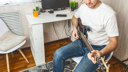 A young man is playing solo an electric guitar at home.