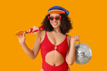 Beautiful woman in swimsuit, with umbrella and disco ball on yellow background