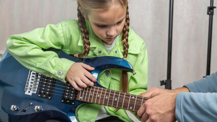 Music teacher and teenage student girl sitting on sofa learning to play on guitar in private lesson...