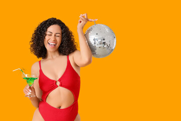 Naklejka premium Happy woman in swimsuit, with cocktail and disco ball on yellow background