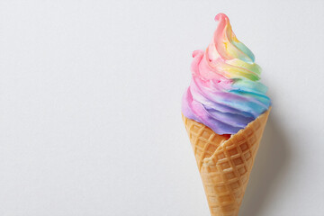 Colorful rainbow soft serve ice cream cone on a plain background ready to be enjoyed