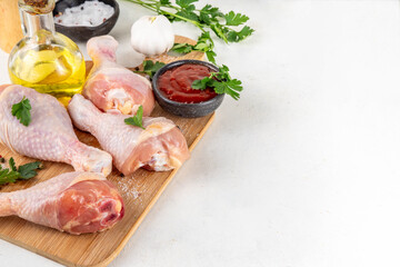 Chicken meat preparation background, raw chicken legs ready for grilling, with spices, salt, pepper, olive oil, garlic and marinade or sauce. Grilll and bbq season cooking background, copy space