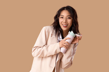 Young Asian businesswoman with thermos on beige background