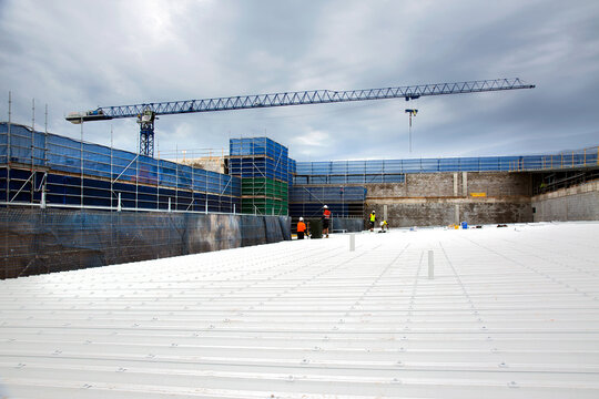 Looking across a metal roof at construction workers on an industrial building site