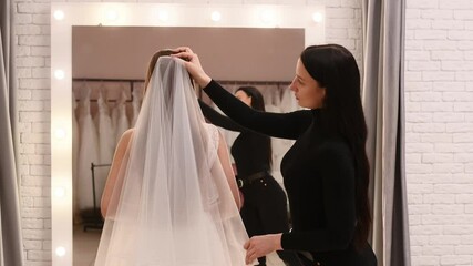 young bride in a wedding salon tries on a dress in front of a large mirror with the help of a consultant. wedding boutique, planning and preparation for the celebration. Wedding consultant, help for t