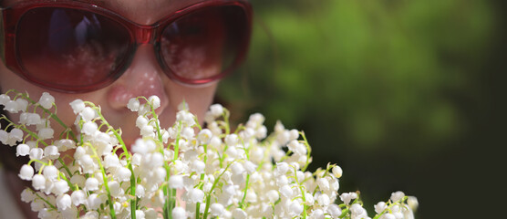Caucasian woman in sunglasses smelling white lily of the valley flowers. Summer scent of flowers.
