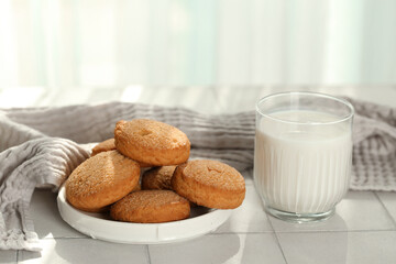 Plate with sweet cookies and glass of fresh milk on white tile table