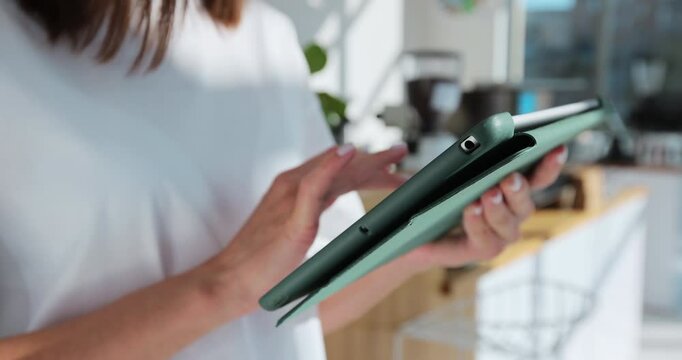 Close up of young woman barista using digital tablet at counter and taking orders from clients in cafe.