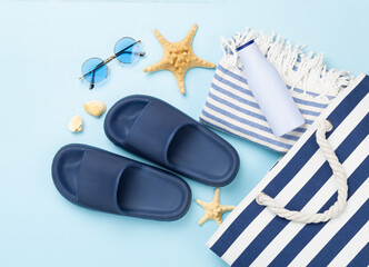 Blue beach bag with summer accessories on color background, top view