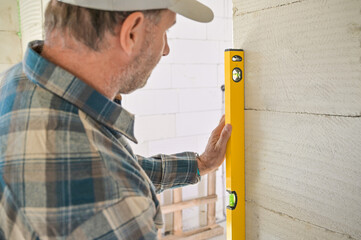 A construction worker carefully uses a level tool to ensure the wall is perfectly vertical,...