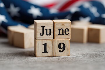 Wooden blocks spelling out June 19th, resting on a gray surface with a blurred American flag in the background.