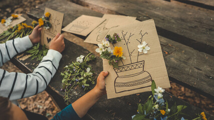 Children creating handmade flower crafts using cardboard, drawing vases and attaching real spring...