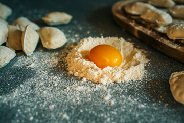 Raw egg yolk in a mound of flour on a kitchen counter, surrounded by homemade dumplings ready for...
