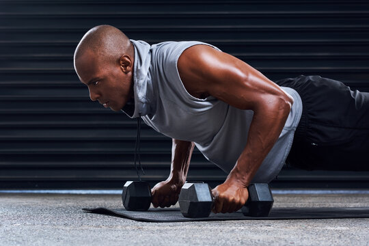 Fitness, push ups and black man with dumbbells in gym for cardio workout, endurance challenge or muscle growth. Power, wellness and athlete on mat for performance, training or strength exercise
