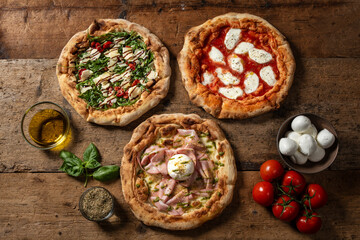 Overhead shot of three different pizzas with various toppings, displayed on a rustic wooden surface.