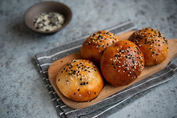 Yeast dough pies with sesame seeds on a wooden board