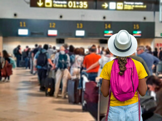 Tourist girl waiting in line to check in baggage at crowded airport counters.