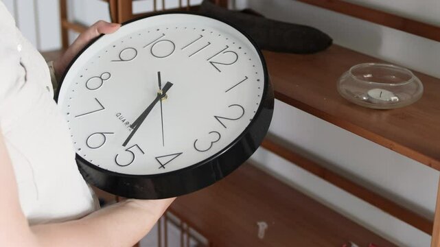 Woman hands setting time on analog black clock.