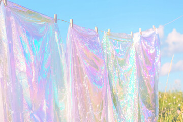 Shimmering iridescent fabrics hang on a clothesline, reflecting sunlight under a clear blue sky.