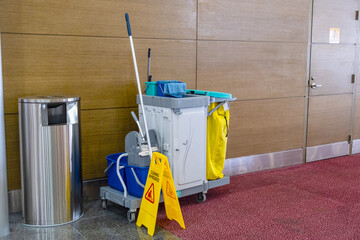 Janitorial cleaning cart with mop, bucket, and caution sign in a commercial building hallway. The...