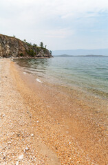 Lake Baikal on quiet summer day. Landscape of shore of Small Sea with sandy and pebble beach and clean transparent water near Olkhon Island. Summer travel and vacation. Natural seaside background