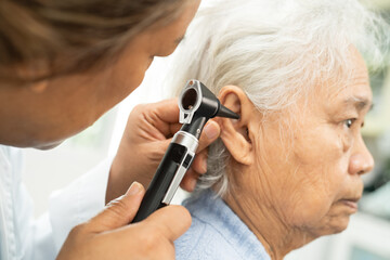 Audiologist or ENT doctor use otoscope checking ear of asian senior woman patient treating hearing loss problem.