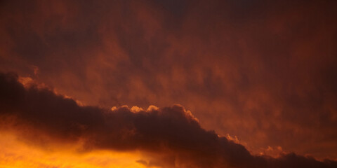 Intense sunset sky featuring deep orange and red tones with dark clouds illuminated from below, creating a dramatic and moody atmospheric background