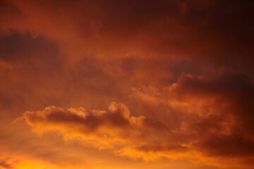 Dramatic sunset sky filled with glowing orange, red, and golden clouds casting a warm, intense light across the horizon and atmosphere