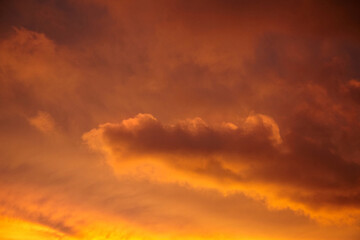 Sunset sky featuring soft layered clouds illuminated by golden and orange tones, creating a serene, radiant, and atmospheric natural background
