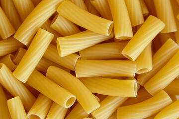 Uncooked tortiglioni pasta shown in detail, featuring short ridged cylindrical shapes with...