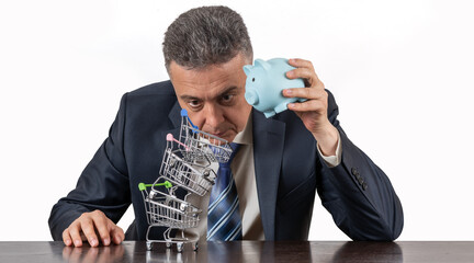 A middle-aged man in a business suit, piggy bnk  and a pyramid of empty miniature supermarket trolleys