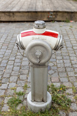 Fototapeta premium Fire hydrant with red and white color scheme stands on cobblestone street, showcasing urban infrastructure and public safety features