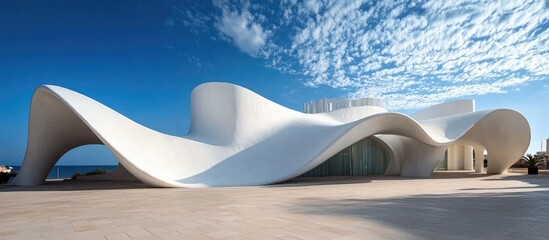 Modern white wave-shaped building near ocean under blue sky.