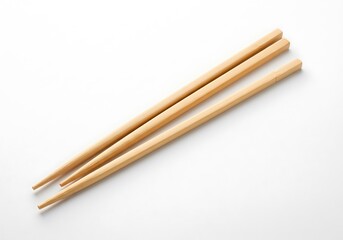A close up of two wooden chopsticks lying diagonally on a plain white surface in bright light