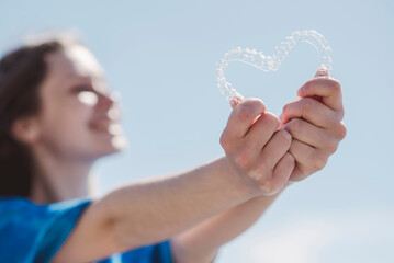 Dental care. Smiling beautiful woman holding heart-shaped aligners. Plastic retainers for teeth alignment.
