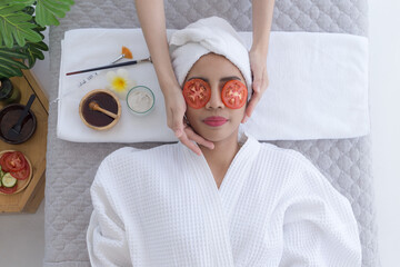 Relaxed young asian woman getting eye nature treatment by tomato at spa salon. Wellness and healing concept.