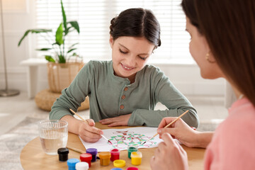 Girl and her mother drawing family tree with paints at wooden table indoors