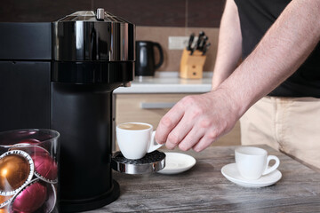 Early in the morning, a man makes espresso coffee in a capsule coffee machine in his home kitchen.