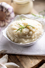 Aromatic garlic paste in a bowl laid on rustic kitchen cloth with bulbs and peeled cloves and rosemary
