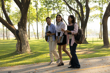 Three women are walking down a path in a park, each with a book in their hands. They seem to be discussing something, possibly related to their studies
