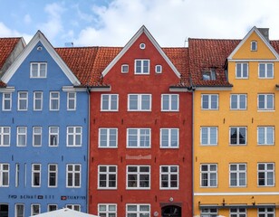 Fototapeta premium Three colorful European-style buildings with gabled roofs, red tile roofs, and many white windows under a cloudy sky.
