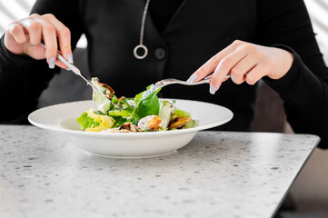 A person enjoys a fresh salad with leafy greens, croutons, and dressing, using a fork and knife at a stylish dining setting. Healthy eating, balanced nutrition, and lifestyle concept.