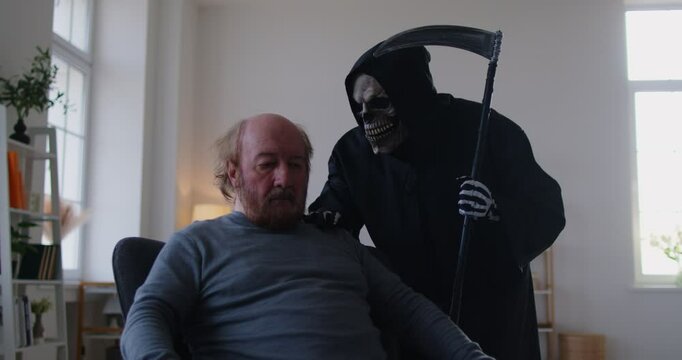 Scared elderly man sitting in chair at home while creepy grim reaper figure with scythe leaning over his shoulder. Frightened senior male sensing fear and approaching end, feeling proximity of death.