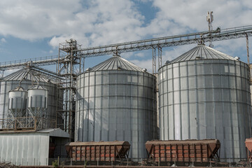 Large metallic silos feature prominently at a grain storage facility amidst a cloudy sky and...