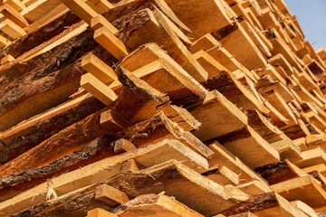 Wooden planks are neatly stacked, showcasing their natural textures and patterns under bright sunlight in a rural lumber yard