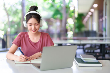 Asian Woman Studying Online with Laptop and Headphones Taking Notes for Education Success College or University Academic Growth