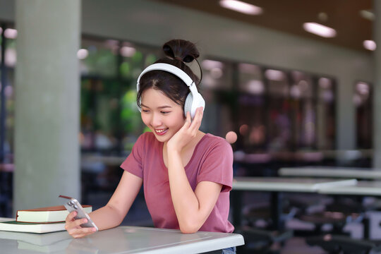 Asian Student Girl Enjoying Mobile App Learning with Headphones in University Library Smiling Reading Social Media Staying Connected
