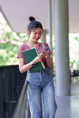 Asian young female student learning checks social media and reads on her mobile phone after studying with book